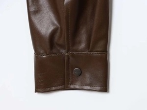 Detail of dark brown leather jacket sleeve showing pebbled texture and metal snap button