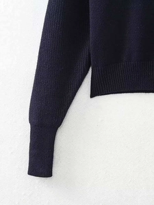 Détail d'un pull en maille bleu marine avec poignets et ourlet côtelés sur fond blanc