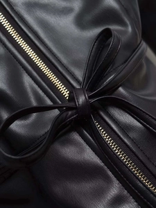 Detail of black faux leather jacket featuring a metal zipper and decorative waist bow