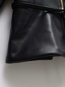 Macro shot of black pebbled leather texture with golden zipper and belt detail on jacket