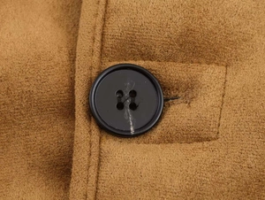 Détail macro du tissu en daim marron présentant un bouton noir à quatre trous et des coutures