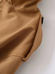 Detail of khaki trench coat featuring twill fabric texture, side pocket, and black button
