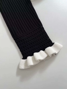 Detail of black ribbed knit sleeve featuring white ruffled cuffs and hollow-out lace patterns