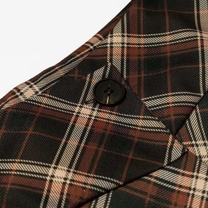 Détail du tissu à carreaux marron et d'un bouton noir sur la jupe plissée