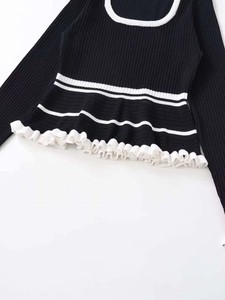 Detailed view of black ribbed knit sweater featuring white contrasting edges and ruffled hem