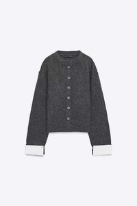 Detail of dark grey knit cardigan with round neck and white contrast folding cuffs