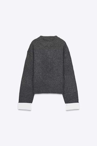Detail of grey crewneck knit sweater featuring oversized white contrasting cuffs