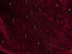 Macro detail of burgundy velvet fabric with sparkling black rhinestone embellishments