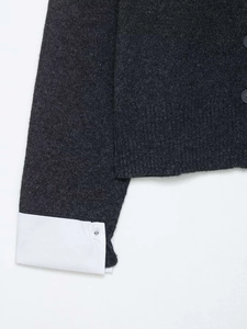 Detail of grey knitted cardigan with white shirt cuff contrast and button textures