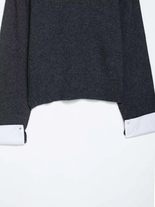 Close-up of contrast knit sweater hem with white shirt cuff details and single button