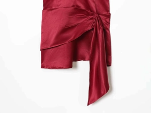 Detail of burgundy satin dress showing side knot design and layered ruffles