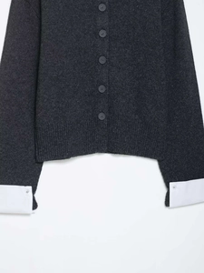 Detail view of dark grey knit cardigan with white shirt cuff splicing and small buttons