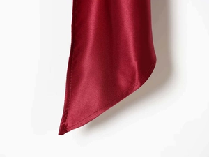 Close-up of burgundy satin fabric showing refined hem stitching and silky smooth texture