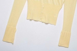 Detail of pale yellow knit cardigan featuring small buttons and ribbed cuff texture