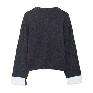 Detailed view of dark grey knit sweater with white shirt cuffs and button accents