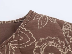 Close-up of brown quilted jacket with white wavy embroidery and heavy fabric texture