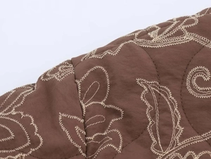 Macro shot of dark brown quilted fabric with beige floral wavy embroidery and fine texture