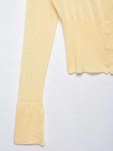 Detail of light yellow knit cardigan featuring fine texture and small translucent buttons
