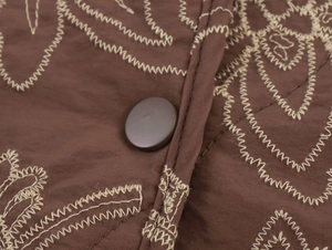 Macro detail of brown quilted jacket with beige embroidery and large matte button