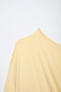 Macro detail of asymmetric neckline and delicate beadwork on light yellow knitwear