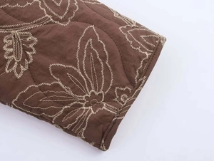 Detailed view of white floral embroidery on dark brown quilted jacket sleeve