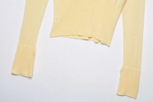 Detail of light yellow knit top featuring elegant buttoned cuffs and wavy lettuce hemline