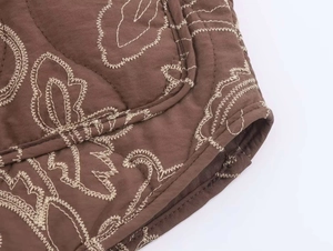 Close-up of dark brown quilted jacket featuring intricate paisley embroidery and detailed hem