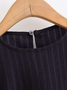 Detail of a black shirt with pleated texture and back keyhole closure on a hanger