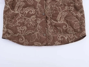 Detail of brown quilted jacket hem featuring white paisley embroidery and patch pockets