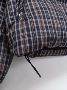 Detail of plaid quilted jacket featuring metal zipper pocket and adjustable drawstring hem