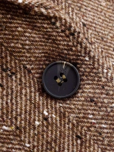 Detailed macro view of heavy brown herringbone weave fabric and premium resin button