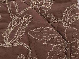 Close-up of diamond quilting and white paisley embroidery on brown fabric jacket