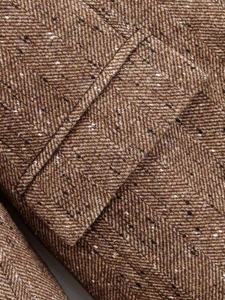 Detail shot of brown herringbone tweed blazer showing premium fabric texture and pocket seam