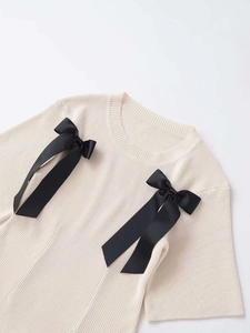 Detailed view of cream knit sweater featuring elegant black grosgrain ribbon bows decoration
