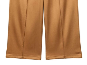 Detail of high-waist wide-leg pants showing brown satin fabric texture and sharp center crease