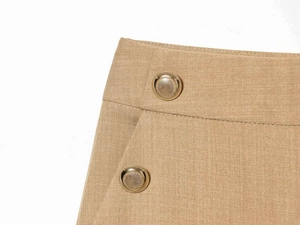 Detail of high-waisted trousers with twill texture and decorative gold metal buttons