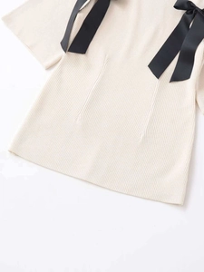 Detail of cream rib-knit sweater featuring black decorative bow ribbons on the shoulders
