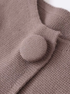 Makroaufnahme der Rippstrick-Textur und stoffbezogener Knöpfe an der braunen Strickjacke