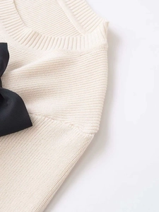 Detail of cream knit sweater showing round neckline and large black ribbon bow on shoulder