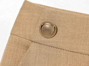 Macro view of gold textured metal button on khaki twill high-waist trousers