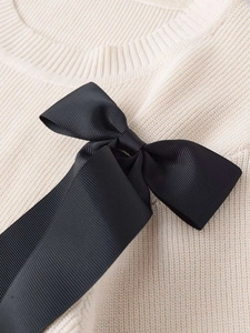 Close-up of cream knit sweater featuring fine vertical ribs and a large black satin bow