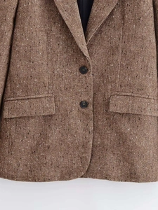 Close-up of brown herringbone tweed blazer with black buttons and detailed fabric texture