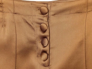 Detailed close-up of brown satin wide leg trousers with silk-covered button fly