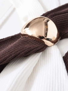 Detail of golden hemispherical buckle on dark brown and white ribbed knit fabric vest