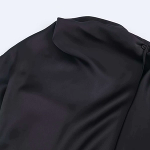 Détail de la robe en satin noir avec col montant plissé et bouton délicat assorti