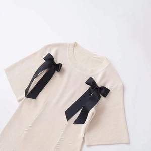 Short sleeve beige knit top with contrasting black ribbon bows on a ribbed texture surface