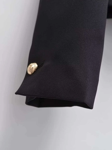 Close-up of black blazer sleeve with textured fabric and vintage gold embossed button