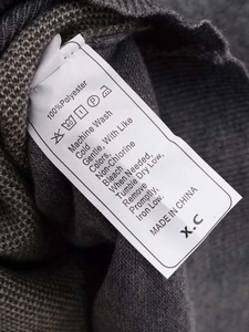 Close-up of fabric care label on gray-brown diamond knit sweater showing 100% polyester
