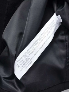 Detail of white fabric care label on black cotton jacket showing 100% cotton material