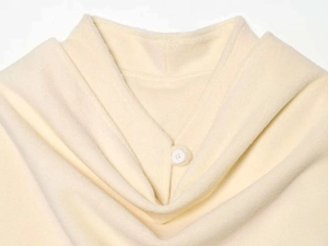 Detailed close-up of cream knit capelet showing soft fabric texture and single button closure